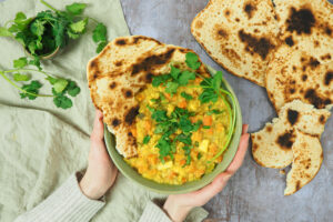 Linsencurry mit Süßkartoffel angrichtet in einer Schüssel mit Koriander und Naan-Broten.