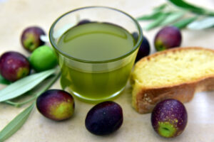 Grünes Olivenöl in Glas. Drum herum Oliven und Baguette.