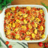 Gnocchi und Gemüse in Tomatensoße überbacken mit Käse. Auflaufform auf Holzuntergrund, dekoriert mit frischen Kräutern und Tomaten.