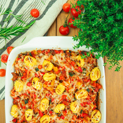 Gnocchi und Gemüse in Tomatensoße überbacken mit Käse. Auflaufform auf Holzuntergrund, dekoriert mit frischen Kräutern und Tomaten. 