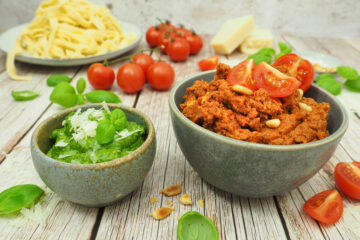 Basilikumpesto und Tomatenpesto angerichtet mit Parmesan und Pinienkernen. Im Hintergrund selbstgemachte Nudeln